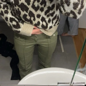 Olivgröna bootcut byxor med fickor - Snygga olivgröna byxor med bootcut-ben och markerade sömmar framtill. Byxorna har två fickor med lock och knapp framtill samt klassisk knappgylf. Tillverkade i ett mjukt bomullstyg med lite stretch för extra komfort. Från H&M, slutsålda