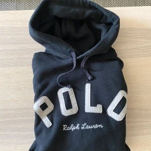 Svart hoodie från Polo Ralph Lauren - Svart hoodie från Polo Ralph Lauren med snyggt tryck på framisdan. Storlek S