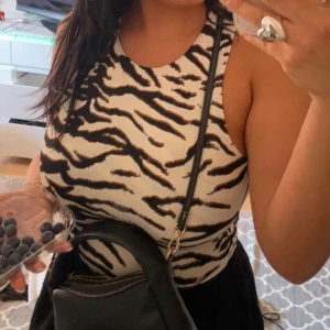 Zebramönstrad ärmlös linnetopp - Snygg ärmlös linnetopp med zebramönster i svart och vitt. Toppen har en tight passform och rund halsringning, perfekt för dig som vill sticka ut med ett djuriskt print. Superenkel att matcha med både jeans och kjol.