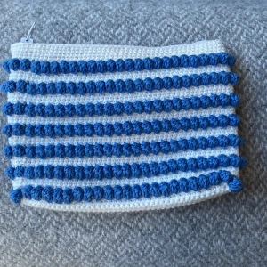 Randig virkad necessär i blått och vitt - Superfin hemmagjord necessär med blå och vita ränder och bubblig struktur. Väskan har dragkedja upptill och är fodrad på insidan. Perfekt för småprylar eller smink. Höjd: 12, bredd: 17. Du står för frakten, vid mer info skriv