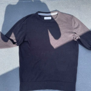 Svart tröja från Pier One - En stilren svart tröja från Pier One med rund halsringning och ribbade muddar. Tröjan är enkel och passar perfekt till jeans eller chinos. Tillverkad i mjuk bomull som känns skön mot huden. Klassisk modell med lång ärm och diskret design.