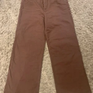 Bruna raka byxor i bomull - Säljer ett par bruna byxor med rak passform och klassisk look. Byxorna är tillverkade i mjuk bomull och har en enkel design utan synliga detaljer. Perfekta för dig som gillar en clean och stilren vibe.
