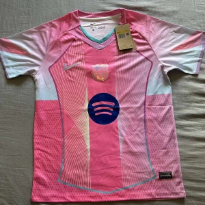 Barça x Nike rosa fotbollströja S - Säljer en FC Barcelona x Nike fotbollströja i rosa och ljusblått med vita detaljer. Tröjan har korta ärmar, V-ringning och är tillverkad i Dri-FIT-material. Framsidan har klubbmärke, Nike-logga och Spotify-logga. Snyggt grafiskt mönster och modern look.