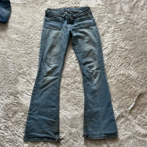 Levis jeans - Säljer ett par blå bootcut jeans med klassisk femficksdesign och slitna benslut för en cool, avslappnad vibe. Jeansen har låg midja och är tillverkade i mjukt denim. Perfekta för dig som gillar en retrostil med edge.