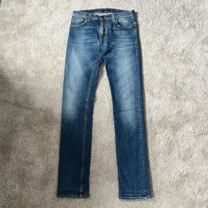 Nudie Jeans Thin Finn - Säljer ett par klassiska blå skinny jeans från Nudie Jeans med en super snygg tvätt och ikonisk mörkblå brodyr mot det ljusblå på bakfickorna.  Otroligt snygga detaljer med nudie jeans stämplat på! Storlek: W31 L36. Slim jeans. Skriv vid minsta intresse och fråga gärna om mått eller bilder, passform etc! Ett måste att ha i din garderob! Fin kvalitet! MVH DC🔹