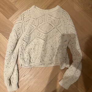 Beige stickad tröja med hålmönster - Säljer en beige stickad tröja med snyggt hålmönster och rund hals från Zara. Tröjan har lång ärm och är lite croppad i modellen, perfekt för att ge en chill och trendig vibe. Mjuk och skön, passar till jeans eller kjol för en cool look.