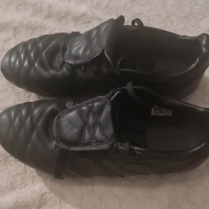 Addidas predetor 2024 - Säljer ett par svarta fotbollsskor från Adidas med klassisk design och snörning. Skorna har quiltad ovandel i skinn och dobbar på sulan för bra grepp på planen. Perfekt för dig som vill ha stilrena och funktionella skor till träningen eller matchen.