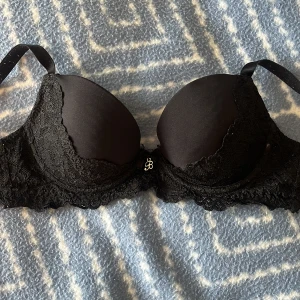 Svart spets-bh - Snygg svart bh från Cubus med  detaljer i spets. Liten metallberlock framtill mellan kuporna. Axelbanden är justerbara och spetsen ger en extra lyxig känsla.💞