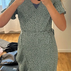 Grön prickig omlottklänning Vero Moda - Snygg grön omlottklänning från Vero Moda i storlek XS. Klänningen har vita prickar, volangdetaljer vid ärmarna och knyt i midjan. Modellen är kortärmad och har en v-ringad omlottfront. PRIS GÅR ATT DISKUTERA 💚💚