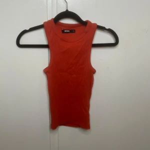Ribbad röd linnetopp från Bik Bok - Säljer en ribbad röd linnetopp från Bik Bok i storlek XS. Toppen är ärmlös med klassisk rund halsringning och har en tight passform. Perfekt att styla med jeans eller kjol för en enkel och snygg look.