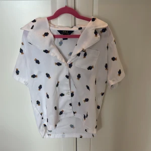Vit skjorta med björnmönster Polo Ralph Lauren - Vit pyjamas skjorta från Polo Ralph Lauren med kort ärm och söt björnmönster över hela tyget. Skjortan har klassisk krage, bröstficka och knäppning framtill. 