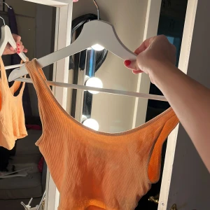 Ribbad orange linnetopp - Snygg ribbad linnetopp i orange med asymmetrisk axel och tight passform. Perfekt för dig som gillar en enkel men trendig look. Tunt och stretchigt material som känns skönt mot huden.