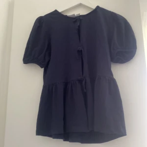 Blå blus med puffärm från Gina Tricot - Supersöt blå blus från Gina Tricot med puffiga korta ärmar och knytningar framtill. och volang nedtill som ger en cool och trendig look. Perfekt att styla med jeans eller kjol för en chill vibe.