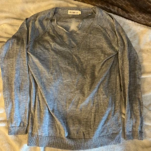 Grå stickad tröja med stjärna Lely Wood - Snygg grå stickad tröja från Lely Wood med v-ringad hals och lång ärm. På ryggen finns en ljusgrå stjärna som cool detalj. Perfekt för dig som gillar enkel stil med en twist. Ribbad kant vid ärmslut och nederkant för extra komfort.