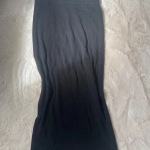 Svart långkjol - Står storlek M men passar för mindre.Säljer en enkel svart långkjol i mjukt bomullsmaterial. Kjolen har en rak och tight passform som sitter snyggt längs kroppen. Perfekt för dig som gillar minimalistisk stil och vill ha en basic kjol i garderoben.