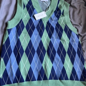 Grön och blå rutig väst från Vailent - Snygg stickad väst från Vailent i storlek XS med gröna och blå nyanser. Västen har ett klassiskt rutig argylemönster och bred ribbad kant vid hals och nederdel. 