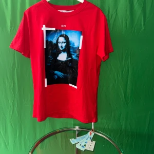 Röd Off-White t-shirt med Mona Lisa print - Röd t-shirt från Off-White med ikoniskt Mona Lisa-tryck framtill och stora vita pilar på ryggen. Klassisk passform, rund hals och korta ärmar. Tillverkad i mjuk bomull, perfekt för dig som gillar streetwear med konstnärlig twist.