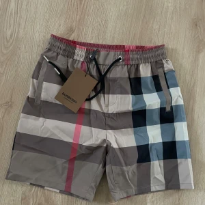 Rutig Burberry shorts med snörning - Snygga Burberry shorts i klassiskt rutigt mönster med beige, svart, vit och röd färg. Modellen har elastisk midja med snörning och praktiska fickor.  Helt nya! Skicka bud!!                                                    Står L i storlek men sitter mer som S/Liten M.