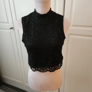Svart crop topp nytt - Oanvänd svart , ärmlös crop top med spetsmönster. Stängs med knapp i nacken. Säljer en likadan fast I vitt. (Lapp bortklippt) Nypris 299 kr