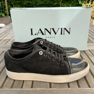 Lanvin skor  - Stilrena svarta sneakers från Lanvin med ovandel i mocka och en glansig, lackad tå. Skorna har vita, tjocka sulor och svarta snören. Perfekta för dig som gillar en clean look med lyxig känsla och unika detaljer.