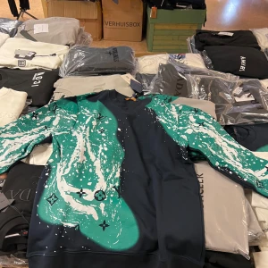 Louis Vuitton svart/grön sweatshirt - Snygg svart sweatshirt från Louis Vuitton med grön och vit splash-design och klassiska LV-loggor. Tröjan är i 100% bomull och har lång ärm. Perfekt för dig som vill sticka ut med en unik och exklusiv look.