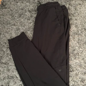 Svarta mjukisbyxor från SOC - Svarta mjukisbyxor från SOC med elastisk midja och dragsko. Byxorna har en enkel och clean look, raka ben och sidofickor. Perfekta för chill eller träning. Materialet är mjukt och bekvämt, troligtvis bomull eller polyester.