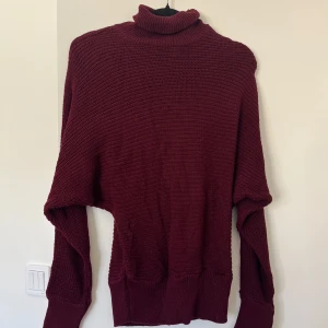 Vinröd stickad polotröja - Mysig vinröd stickad polotröja med långa ärmar. Tröjan har en hög polokrage och breda muddar vid ärmslut och nederkant.