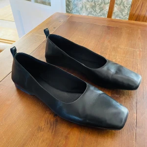 Svarta ballerinaskor från Vagabond - Stilrena svarta ballerinaskor från Vagabond i skinn med fyrkantig tå och låg profil. Skorna har en minimalistisk design med diskret dragflik bak och passar perfekt till både jeans och klänning. Klassisk look med modern twist.