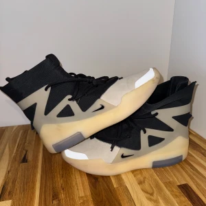 Nike Air Fear of God 1 String/The Question sneakers - Unika sneakers från Nike med futuristisk design i svart och beige. Skorna har högt skaft, snörning och en chunky, transparent sula. Ovandelen är i textil och mocka med coola detaljer och små Swoosh-loggor på sidorna.