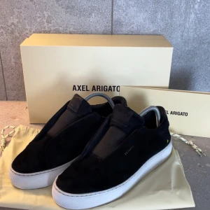  Axel Arigato - Clean 360 laceless - Axel Arigato - Clean 360 laceless. Svart mocka utan snörning. Skorna är i gott skick, 7/10 med endast en defekt (se bild 3). Med skorna skickas orginalkartong och dustbag. Tveka inte på att höra av er! 