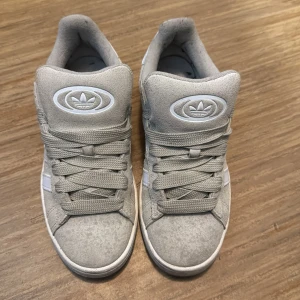 Adidas Campus beige - Snygga Adidas Campus sneakers i beige mocka med klassiska vita ränder på sidorna och vit häl. Skorna har rund tå, platt sula och breda snören. Adidas-logga på plösen och Campus-tryck på sidan. Perfekta för en clean och stilren look. Nypris 1400