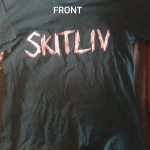 SKITLIV (maniac from mayem) merch M - Svart t-shirt med korta ärmar och trycket 'SKITLIV' i rött på framsidan. Baksidan har text och symboler i vitt och rött. T-shirten har en klassisk passform och rund hals. Materialet ser ut att vara mjuk bomull, perfekt för en edgy och alternativ stil.