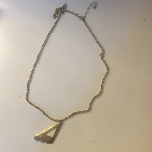 Guldigt halsband med trekantig berlock - Snyggt halsband i guldton med en cool, trekantig berlock som har en öppen mitt. Kedjan är tunn och har justerbar längd. Perfekt för dig som gillar stilrena och moderna smycken med en unik touch.