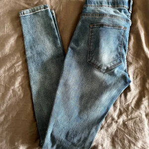 Ljusblå skinny jeans med slitningar - Säljer ett par ljusblå skinny jeans med slitningar på båda knäna. Jeansen har klassisk femficksdesign, normal midja och är i stretchigt denimtyg för en tight passform. Perfekta för dig som gillar en avslappnad men trendig look.