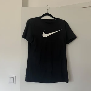 Svart Nike t-shirt  - Svart t-shirt från Nike med klassisk vit swoosh-logga på bröstet.
