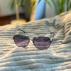 Svarta aviator solglasögon - Snygga aviator solglasögon med tunna svarta metallbågar och mörka, lätt tonade glas. Klassisk pilotform som ger en cool vibe och passar till de flesta outfits. Näskuddar i transparent plast för extra komfort. Har några repor som syns i visst ljus. Är rätt stor i storleken så skulle säga att det passar en vuxen.