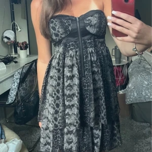 Svart kort klänning från Amisu - Supersnygg svart kort klänning från Amisu med ormskinnsmönster och dragkedja framtill. Axelbandslös modell med markerad byst och utställd kjol. Perfekt för dig som vill sticka ut med en edgy look. Köp via Swish + frakt (ej köp nu) eller direkt via vinted @moa.06 (pga plicks nya avgifterk) 🩷