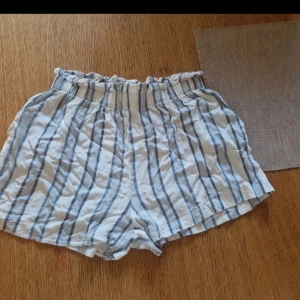 Randiga shorts från H&M, strl 36 - Säljer ett par vita och blå randiga shorts från H&M i storlek 36. Perfekta för varma sommardagar och har en loose fit som ger en chill vibe.