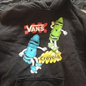Vintage Vans x Crayola hoodie M - Svart hoodie från Vans i samarbete med Crayola. Framsidan har färgglada tryck med blå och grön krita på skateboard, samt loggor i rött, vitt och gult. Klassisk huva och känguruficka. Perfekt för dig som gillar streetstyle och coola prints.