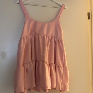 Ljusrosa volangklänning med axelband - Supersöt ljusrosa kortklänning med breda axelband och flera volanglager. Klänningen har en luftig och flowy passform, perfekt för varma dagar. Materialet känns mjukt och lätt mot huden. Ingen synlig logga eller märke. Den är storlek S/M, men lite kort i längden!!<3