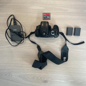 Canon eos 400d kamera. - Säljer en Canon EOS 400D med tillbehör. Kameran levereras med laddare, 8 GB CF Ultra-minneskort, kamerarem och kontakt så att du kan få dina bilder till datorn. Samt 2 batterier, varav 1 köptes nytt i år för 219 kr. HDMI-porten är tyvärr borta och kameran har några repor på undersidan men inget som påverkar bilderna. Men annars är den i gott skick.  Obs: Objektiv ingår ej. Hör av dig vid frågor 😉