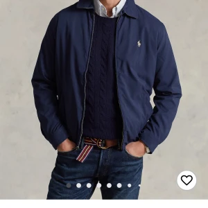 Marinblå vindjacka från Polo Ralph Lauren - Snygg mörkblå vindjacka från Polo Ralph Lauren med klassisk krage, dragkedja och två fickor med knappdetaljer. Jackan har det ikoniska broderade logot på bröstet och är tillverkad i ett lätt och smidigt material. Perfekt för dig som gillar stilren och tidlös look.Jag fick den som en födelsedagspresent och den var för liten för mig så jag tänkte att sälja den istället. Jackan är helt ny. Nypris är 2995kr.