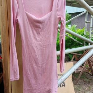 Rosa ribbad klänning från Bik Bok stl M  - Söt rosa kortklänning från Bik Bok i ribbad ekologisk bomull med stretch. Klänningen har lång ärm och en snygg, lite djupare urringning. Perfekt för dig som gillar en enkel men trendig look. Stl M 