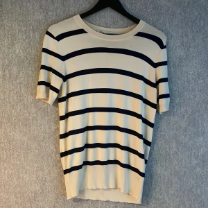 Randig stickad tröja från Zara - Snygg stickad tröja från Zara i vit med mörkblå  ränder. Modellen har rund halsringning och korta ärmar. Materialet är mjukt och stretchigt. 