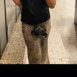 Zebramönstrad långkjol i satin - Säljer en snygg långkjol med zebramönster i beige och svart. Kjolen har en rak och flowy passform som ger en chill och trendig vibe. Materialet är glansigt satin som känns lyxigt och skönt mot huden. Perfekt att styla med boots eller sneakers. Jätteskön att ha på sig, man kan klä upp kjolen men också klä ner den. 