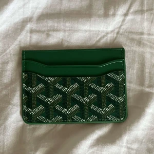 Grön korthållare i skinn - Snygg grön korthållare från deras ikoniska mönster framtill. Tillverkad i skinn med flera kortfack och klassisk logga. Perfekt för dig som vill ha en stilren och lyxig accessoar i fickan.