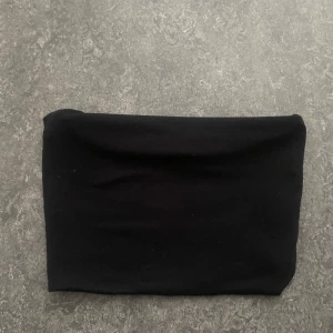 Svart bandeau tubtopp från BikBok - En svart bandeau tubtopp från BikBok i enkel och stilren design. Toppen är axelbandslös och har en tight passform som sitter snyggt på kroppen. Perfekt att matcha med jeans eller kjol för en clean look. Oanvänd, då den aldrig kommit till användning (köpte dubbletter).