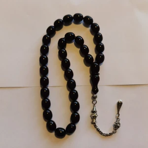 Svart Tasbih pärlhalsband med silverdetaljer - Stilrent halsband med svarta, ovala pärlor och dekorativa silverfärgade detaljer i änden. Perfekt accessoar för dig som gillar klassisk och elegant stil. Kedjan och hängen i metall ger en snygg kontrast till de blanka pärlorna.