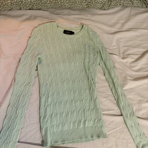 Ljusgrön kabelstickad tröja Morris Lady - Supersöt ljusgrön kabelstickad tröja från Morris Lady i 100% merceriserad bomull. Tröjan har rund halsringning, lång ärm och klassisk kabelstickad struktur. Perfekt för dig som gillar en stilren look.