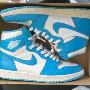 Jordan 1 High UNC  - Säljer ett par Nike Air Jordan 1 i den ikoniska UNC-färgen. Skorna är höga sneakers i blått och vitt skinn med klassisk Air Jordan-logga på sidan, vit sula och blå yttersula. Perfekta för dig som vill sticka ut med en retro basketstil. Skorna är använda och därför går priset att diskutera.